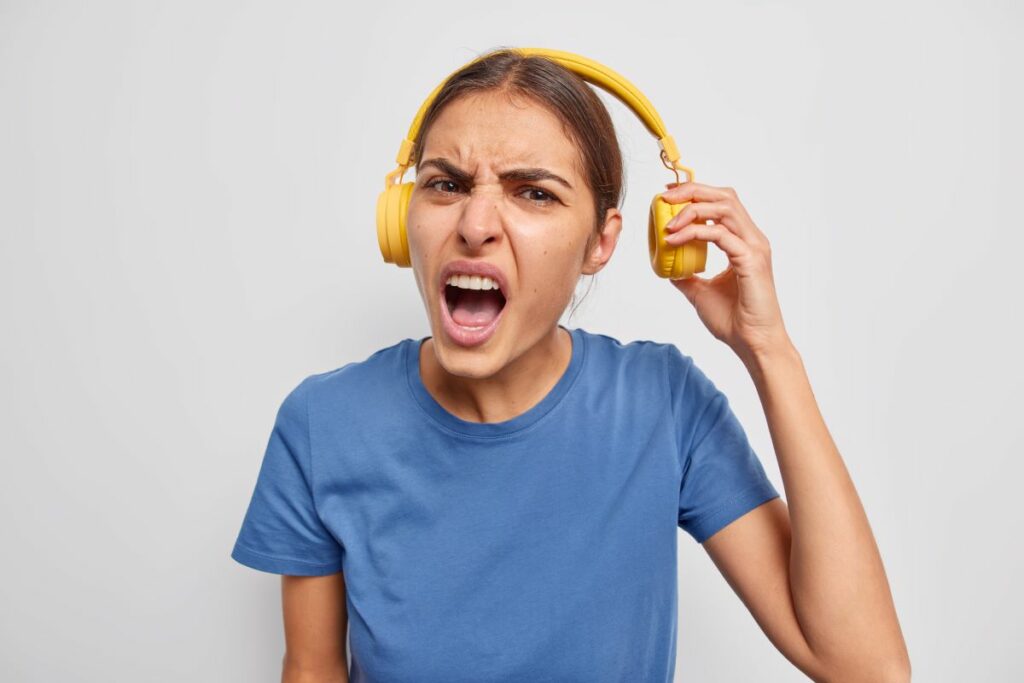 Mulher com expressão de insatisfação, puxando um lado do fone de ouvido que está em sua cabeça.